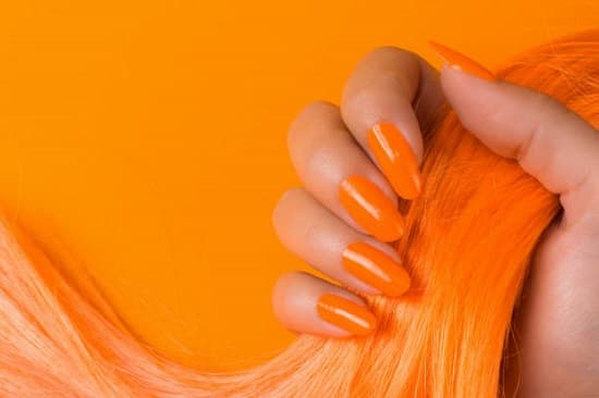 Female hand with orange nails is holding orange hair on orange background.