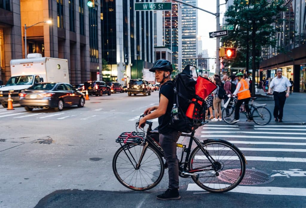 106037428-1563980639750hispanic-courier-on-bicycle-in-crosswalk-in-new-york-city-at-dusk-america-cycle-cycling-male_t20_blnkmv